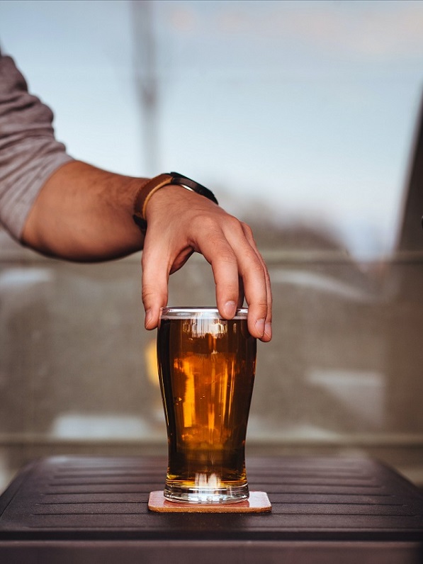 Man with rolled-up long-sleeved T-shirt at picnic table holds top of Pilsner glass from Paykoc Imports without engraving